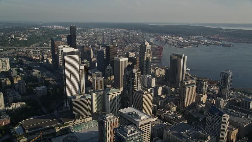 Aerial flyby capturing the tall Downtown Seattle skyscrapers and tracking Two Union Square with an American flag showcasing the patriotic and bustling metropolis during the daytime