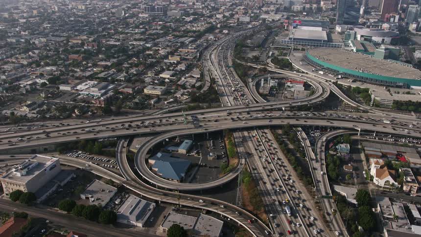 An aerial view of the Los Angeles Convention Center and downtown skyscrapers revealed by orbiting above heavy traffic in the 110 and 10 interchange during rush hour in Southern California