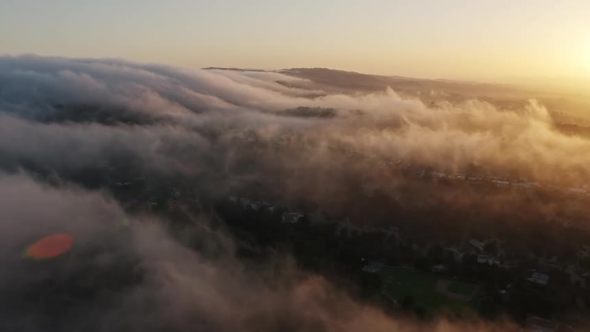 Aerial footage of Studio City California at sunset flying over a marine layer above the hills