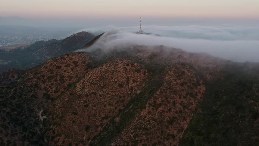 4K aerial footage capturing the marine layer rolling above Hollywood Hills sweeping over the city and valley at dusk