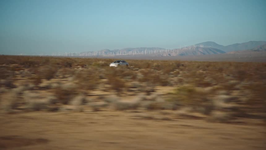 White car drives on a road through the desert plains at daytime