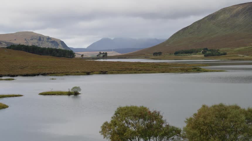 A wide open view of a lake hills and scattered trees is shown from up above