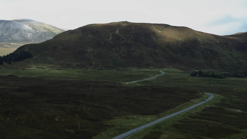 A road winds through a vast field and past rocky hills