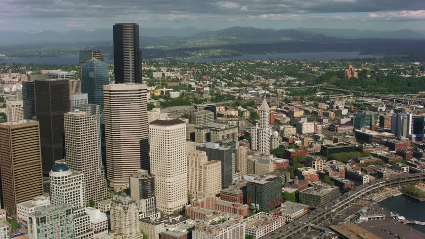 An aerial shot of a city center with tall buildings and greenery before the waterfront