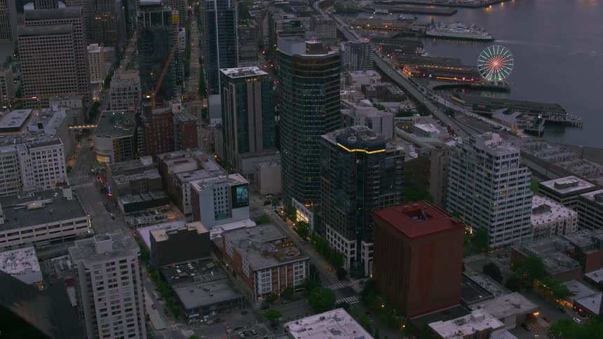 An aerial view of a waterfront downtown city block near a harbor and lit up ferris wheel