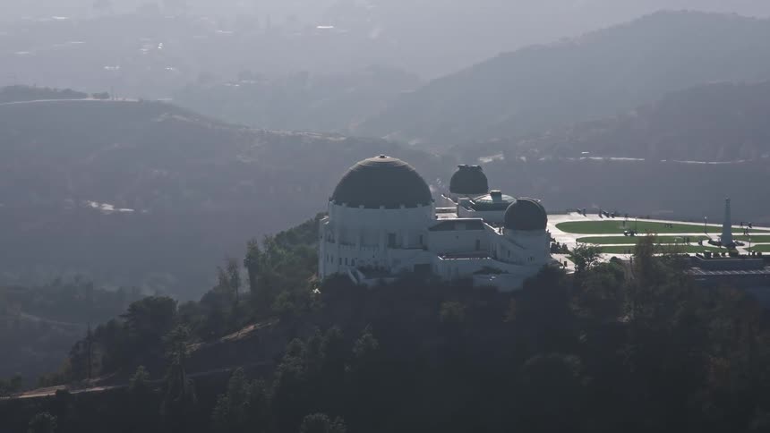 4K aerial footage orbits around the famous Griffith Observatory surrounded by haze and fog on a sunny day in California