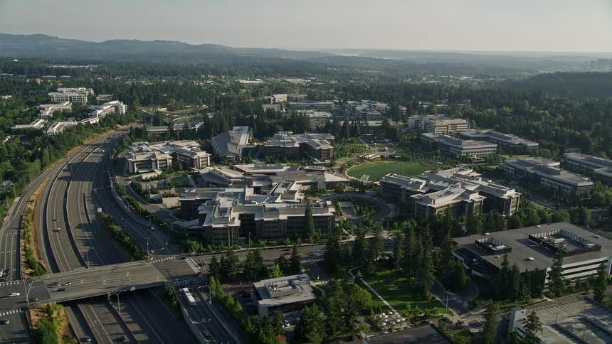Aerial footage of Microsoft Headquarters office buildings orbiting around The Commons soccer field in Redmond Washington during the day showcasing the recreational and industrial activities in the area
