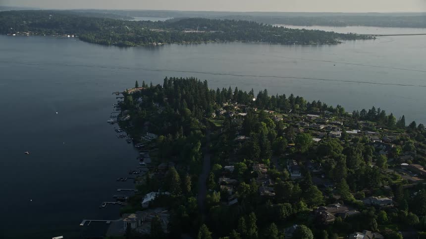 Fly over suburban neighborhoods towards waterfront homes on Lake Washington showcasing the scenic shoreline and sunny residential area in Bellevue Washington