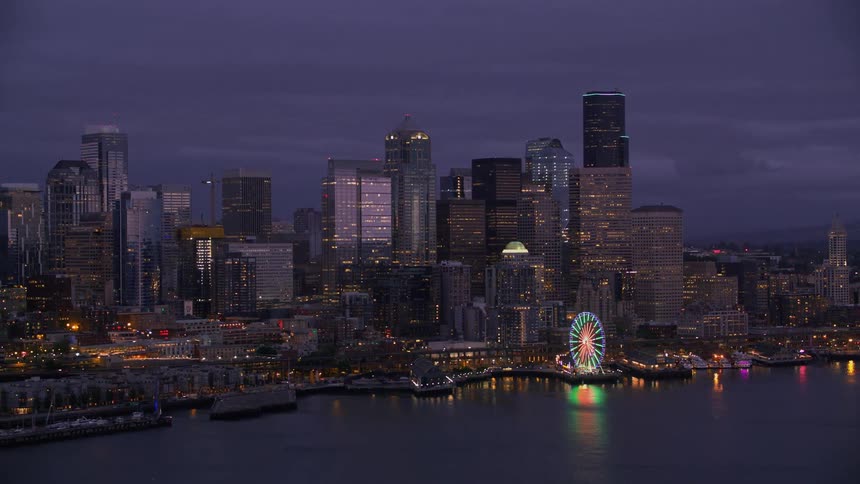 Aerial view of high rise office buildings illuminated ferris wheel near the sea at dusk