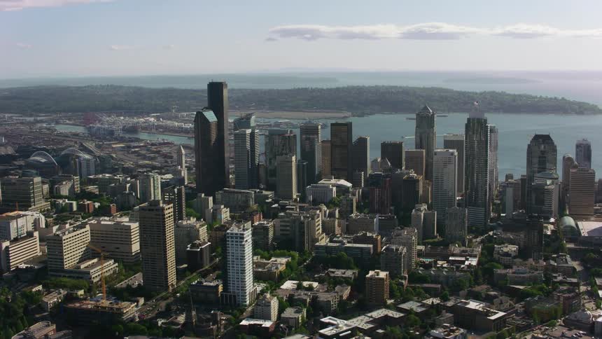 Airplane moves through sky over bay behind downtown skyscrapers