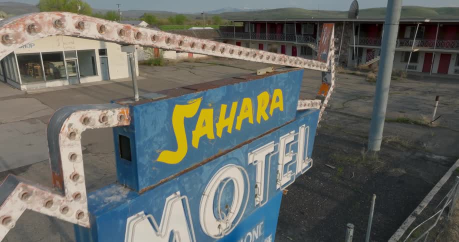 Skimming just above an old and rusted motel sign to reveal an empty and run down parking lot and structures
