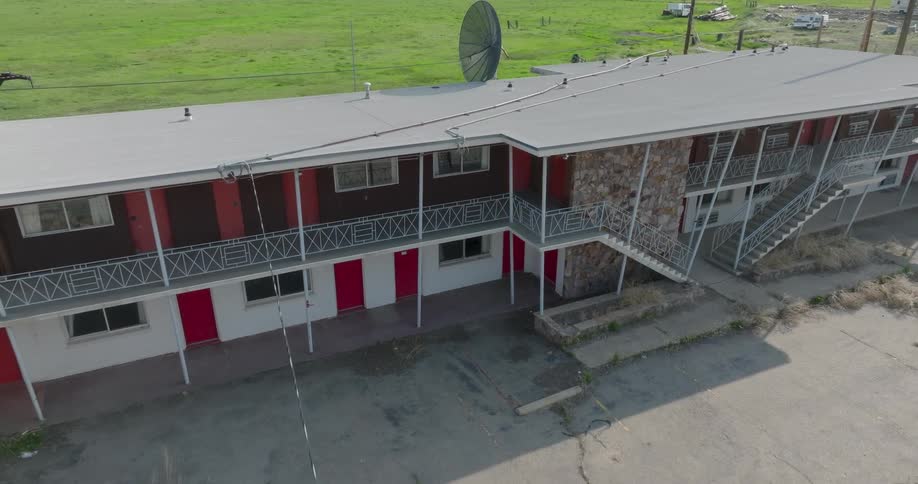 Pullback from an old and dilapidated C-band satelittle TV antenna over a cracked and empty motel parking lot