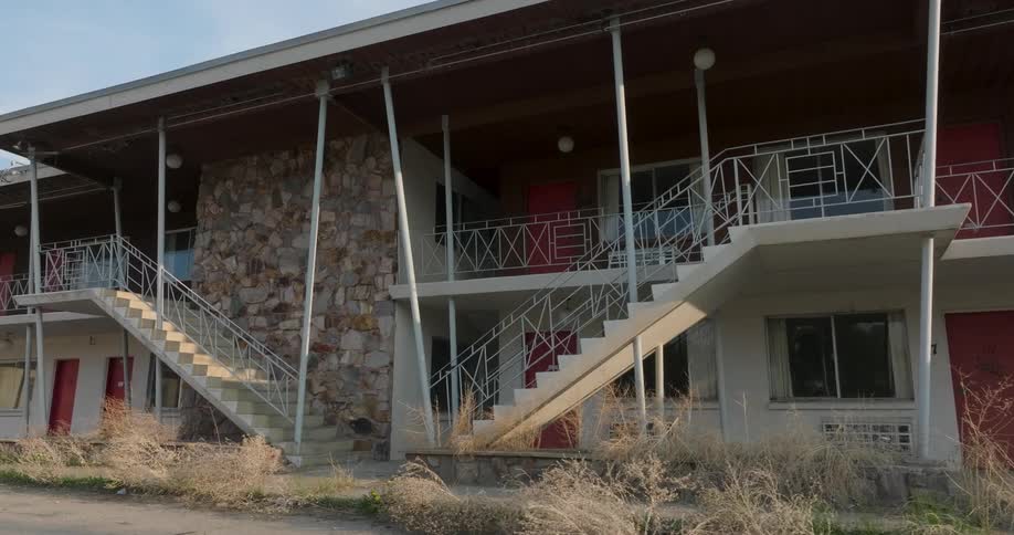 Low orbit around weeds and trash in front of the stairs that lead to the upper levels of a motel