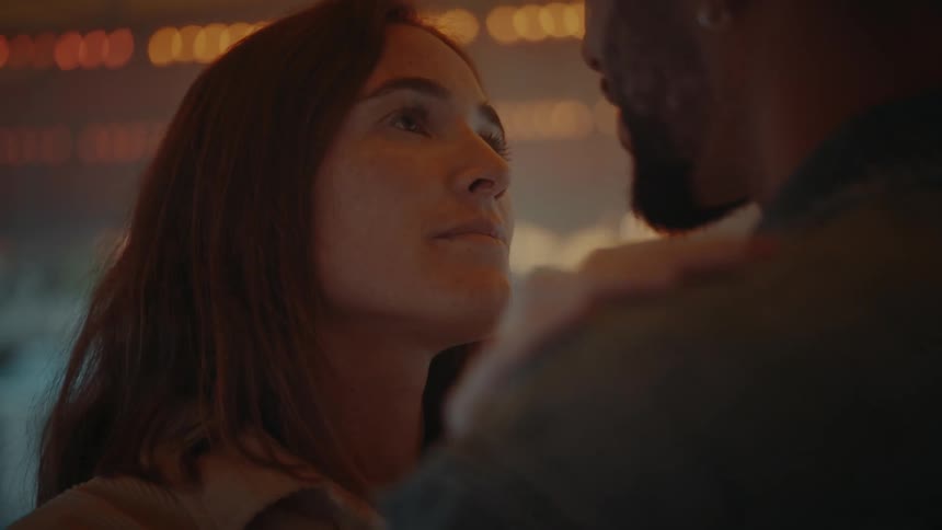 Couple stares into each others eyes while slow dancing under flashing lights in pavilion