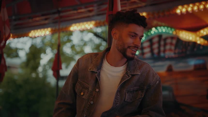A man laughing and smiling while talking to someone in front of him with lights strung behind him flashing