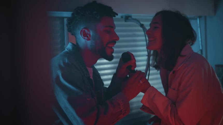 A man and woman sing into a microphone at home
