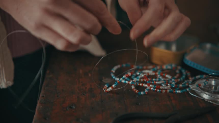 A person is putting beads on the thread