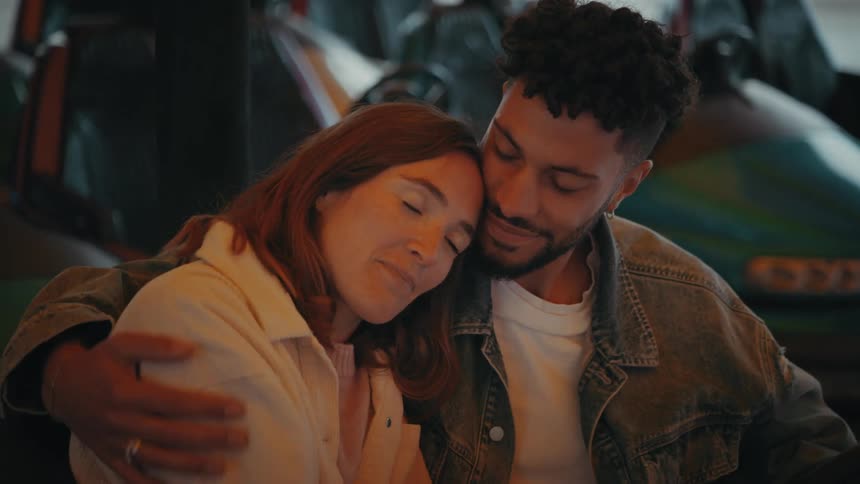 Brown multiracial man and white redhead woman cuddling and caressing inside a bumper car