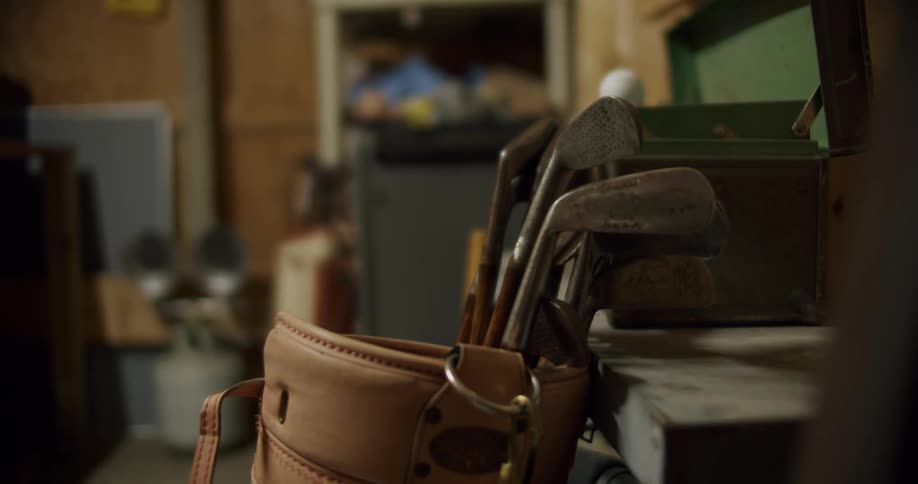 A golf bag with golf clubs inside leaning against a table inside a garage