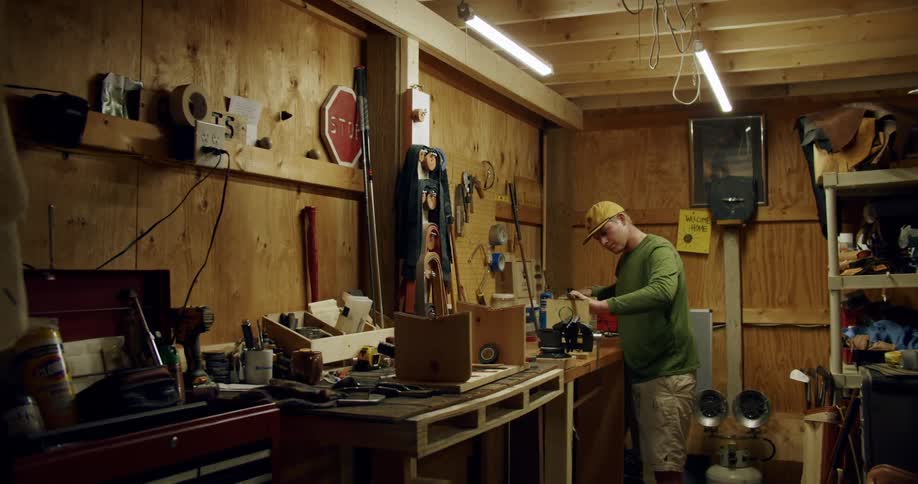 A man is standing over the counter of his workshop and he is focused on the piece he is working on as he moves his hand over the surface