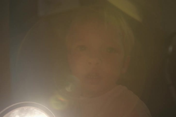 Blonde boy points flashlight while standing in dim room
