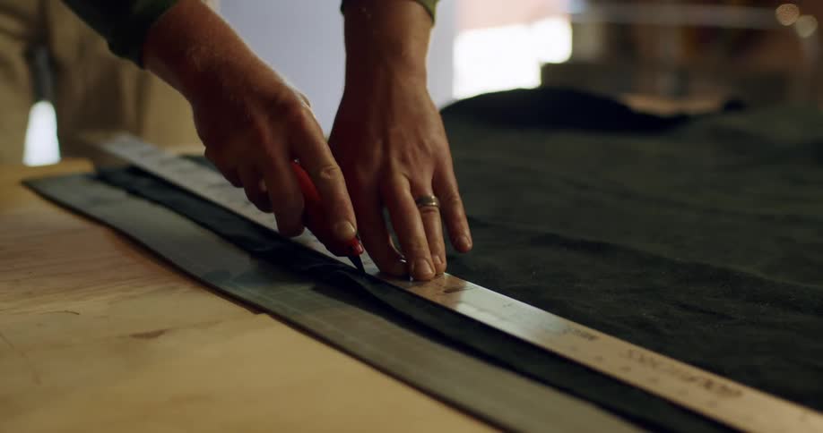 A pair of hands uses a ruler and an xacto knife to cut fabric