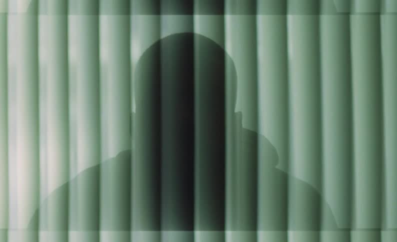 A man sits in front of his window with the blinds drawn