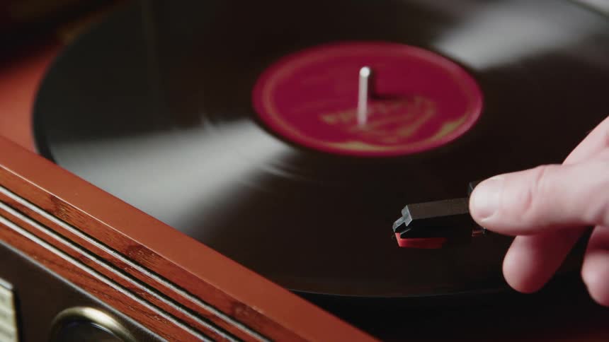A hand moves the needle of a record player to stop a vinyl record from playing