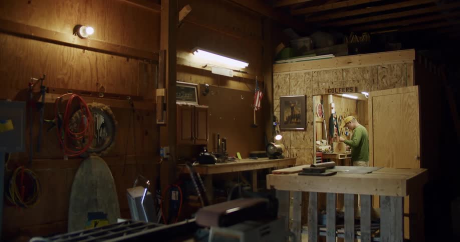 A man works on his workbench inside a work shed build out of plywood in a garage