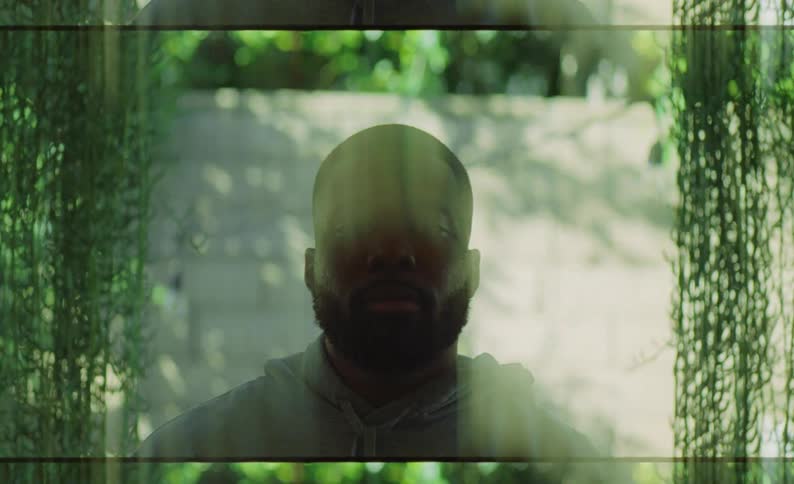 Streaky green blur obscures man standing between vines in shadow