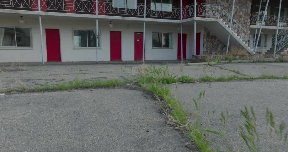 Weeds grow along the cracks of an unused parking lot in front of a closed down motel