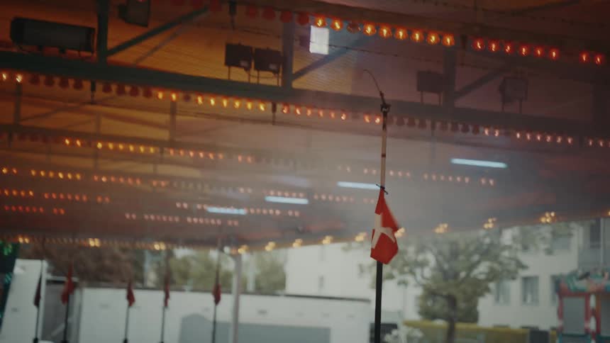 A woman is driving a bumper car in an amusement park as the pole on her car is connected to the electric grid above