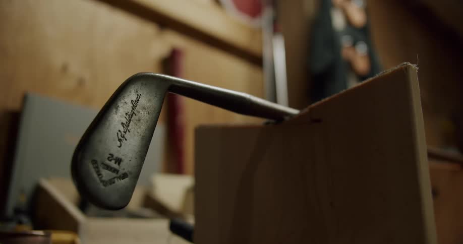 Golf club with engraved lettering rests on wooden board in workshop