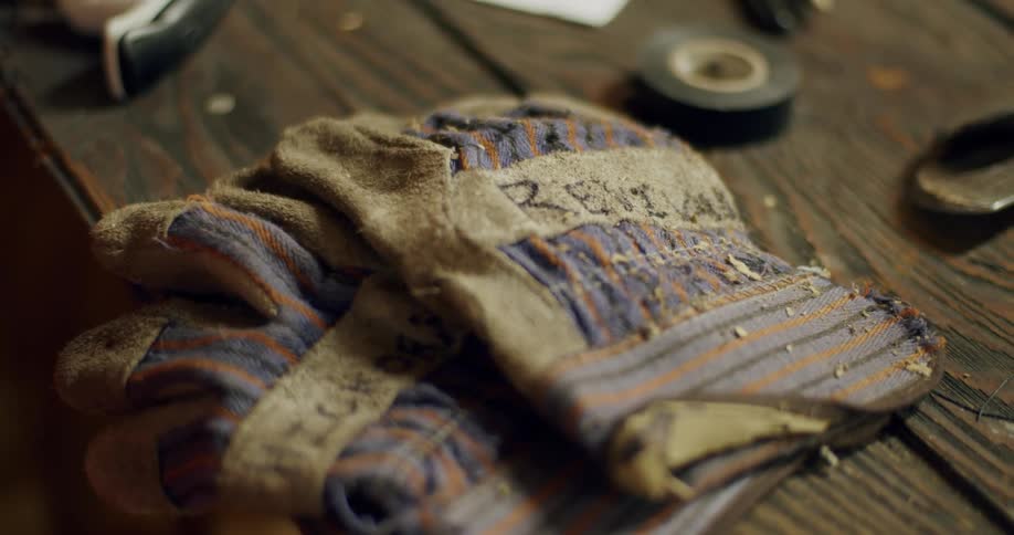 Work gloves sit on wooden workbench near a role of tape