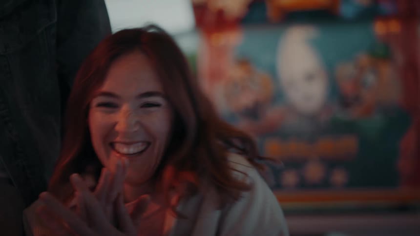 Woman sitting in arcade car laughs and leans against man