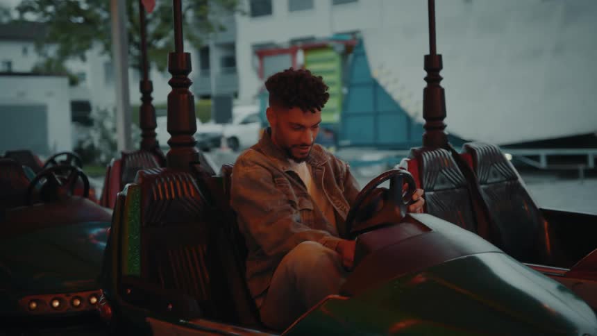 A man smiles as he sits in a bumper car and inserts a token to turn it on
