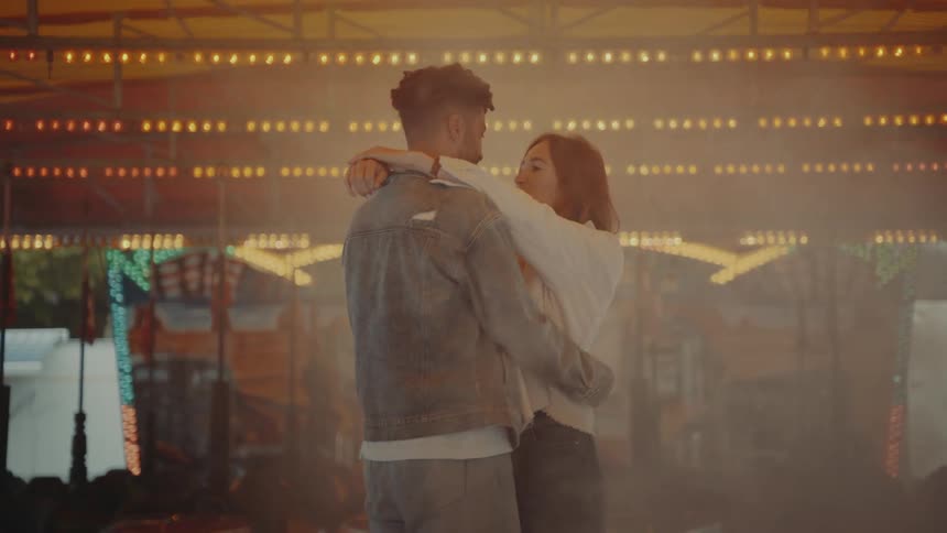 A man and a woman dance in the smoke in front of a carousel