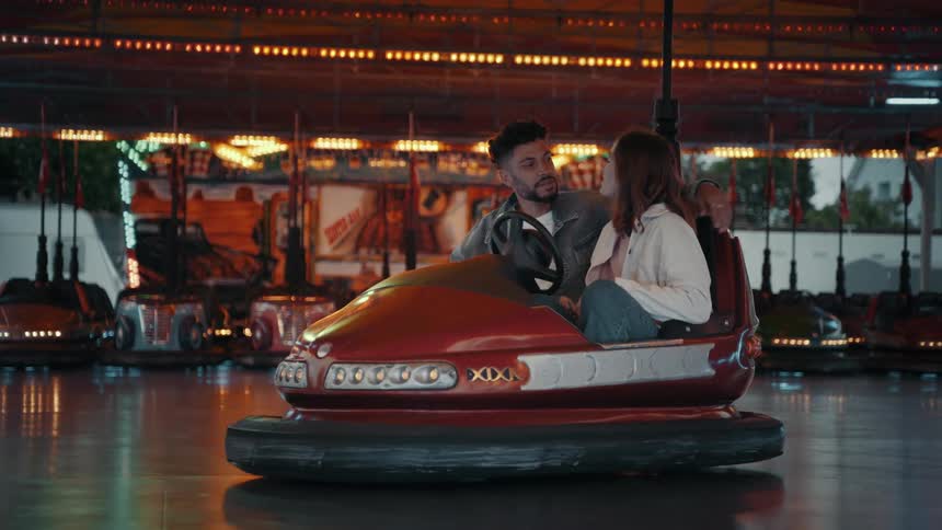 Couple laugh and talk while sharing bumper car at carnival