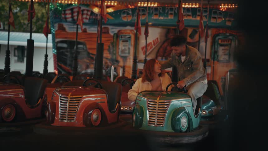 A man and a woman get inside a bumper car at a fair