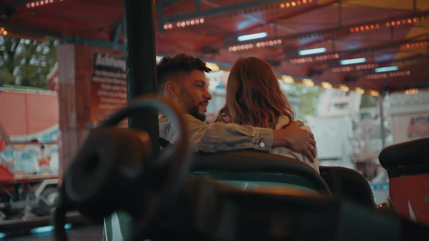 Couple cuddle sitting in open air arcade near bumper car with train car in the background