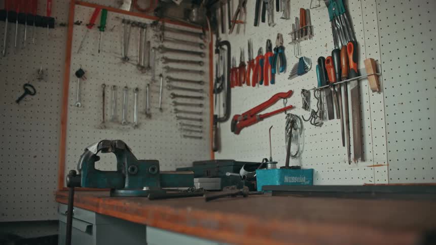 A workshop with a workbench with a lathe and several sets of different tools organized on the wall