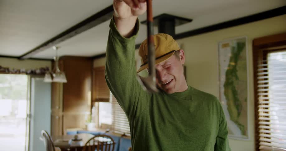 A man in a living room closes an eye and holds up a golf club to check its alignment