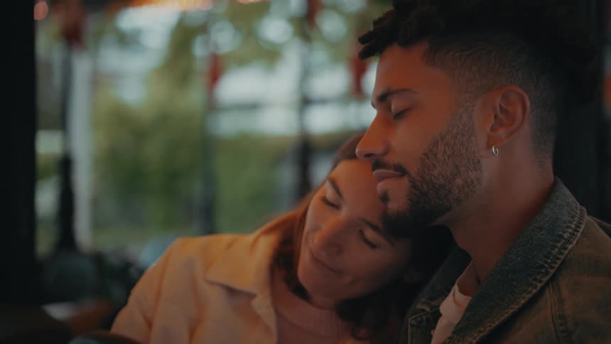 A woman cuddles into the shoulder of a man smiling as theyre both sitting in a bumper car