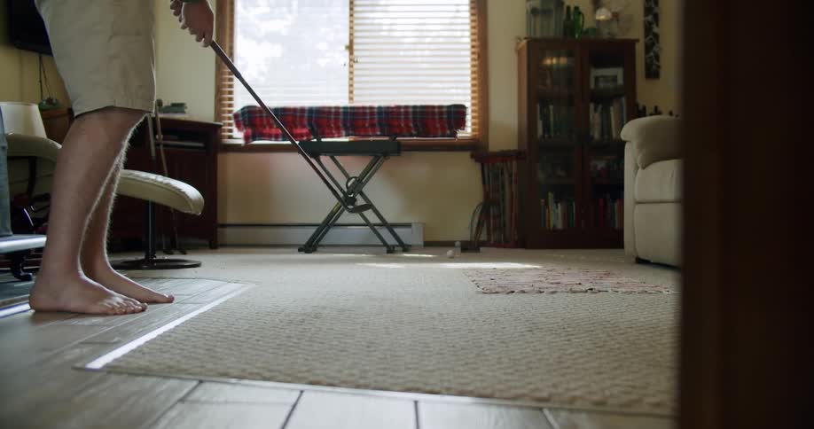 Man with shorts and green shirt plays golf in the living room at home