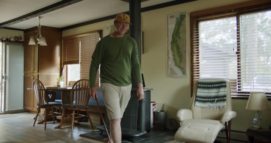 Man with yellow cap green sweatshirt and brown shorts play golf in the living room