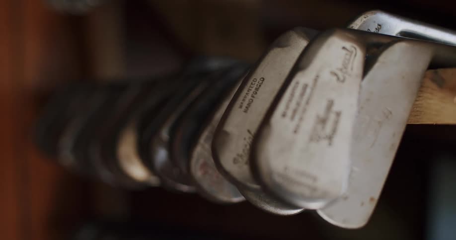 A close up of metal golf clubs resting on a wooden shelf