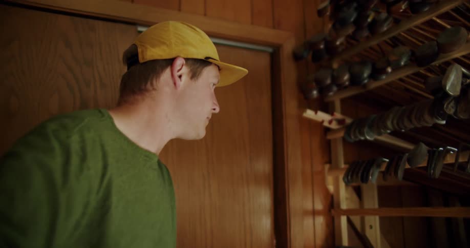 Man removes golf clubs from bag and places them on framework near window