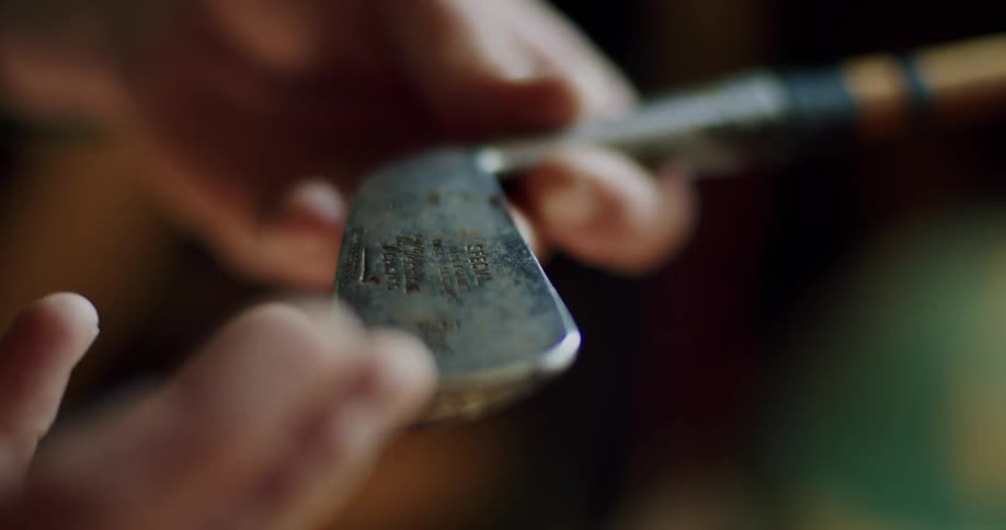 A man runs his finger along the inscription on a golf club