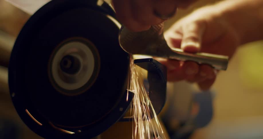 A close up of a person using a grinder on a metal golf club head creating sparks