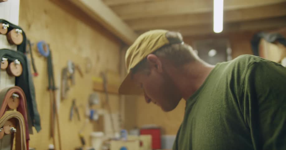 A man wearing a hat walks through a work shed full of tools and made of wood